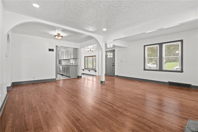 2317 S Maywood Ave, Independence, MO 64052 - unfurnished living room featuring arched walkways, a textured ceiling, wood finished floors, baseboards, and recessed lighting