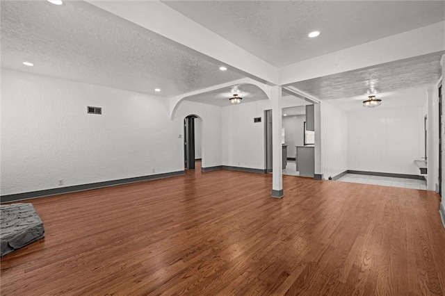 2317 S Maywood Ave, Independence, MO 64052 - unfurnished living room with a textured ceiling, arched walkways, baseboards, wood finished floors, and recessed lighting