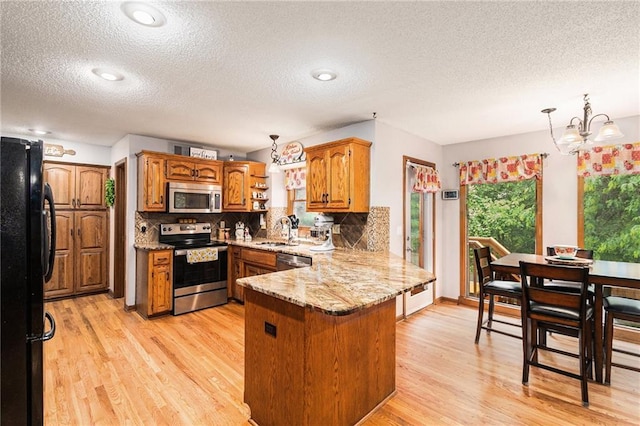 7504 N Palmer Ave, Kansas City, MO 64158 - kitchen with stainless steel appliances, a peninsula, a sink, a textured ceiling, and brown cabinetry