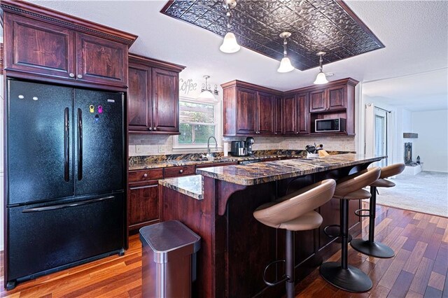 2002 N 29th St, Saint Joseph, MO 64506 - kitchen featuring freestanding refrigerator, stainless steel microwave, wood finished floors, and decorative backsplash