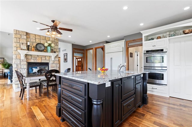 15405 161st St, Bonner Springs, KS 66012 - kitchen featuring stainless steel double oven, a ceiling fan, white cabinets, light wood finished floors, and light stone countertops