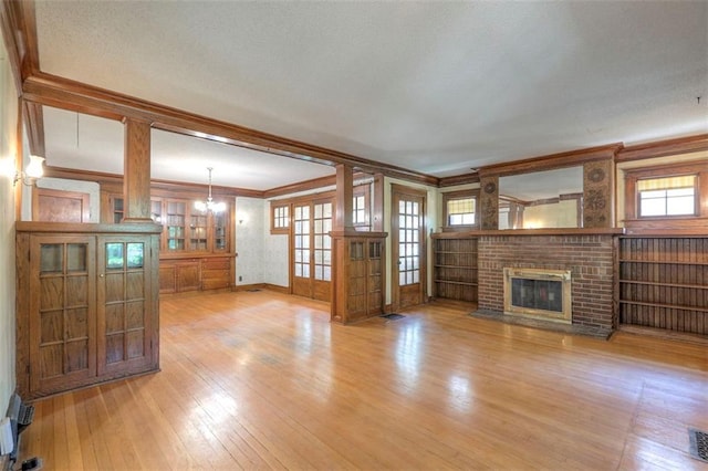 12 W 57th Ter, Kansas City, MO 64113 - unfurnished living room featuring light wood-style flooring, a chandelier, ornamental molding, and a brick fireplace