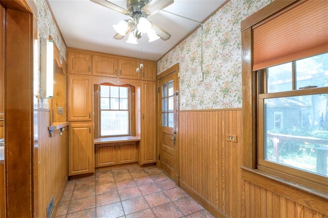 12 W 57th Ter, Kansas City, MO 64113 - doorway with wallpapered walls, plenty of natural light, a wainscoted wall, a ceiling fan, and light stone finish floors