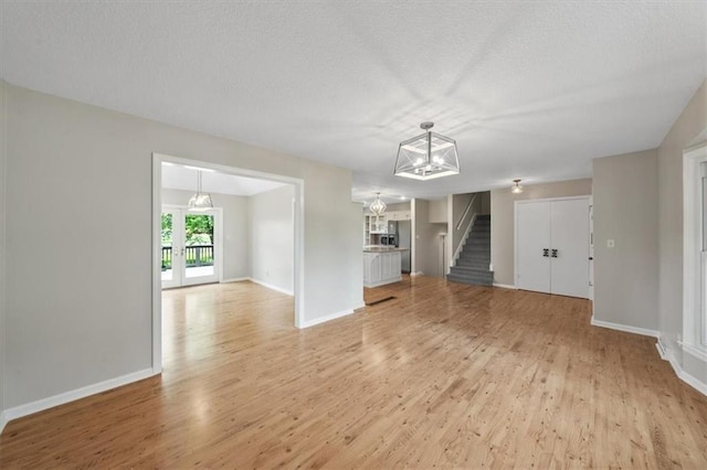 5000 W 96th St, Overland Park, KS 66207 - unfurnished living room featuring a chandelier, light wood finished floors, stairway, baseboards, and a textured ceiling