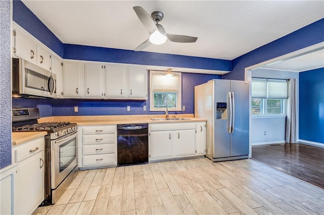 5912 E 98th St, Kansas City, MO 64134 - kitchen with stainless steel appliances, light countertops, a ceiling fan, white cabinets, and light wood-type flooring