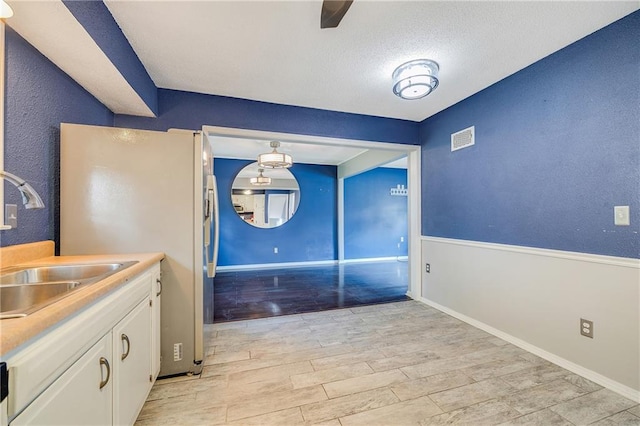 5912 E 98th St, Kansas City, MO 64134 - kitchen featuring white cabinets, a sink, light wood-style floors, freestanding refrigerator, and light countertops