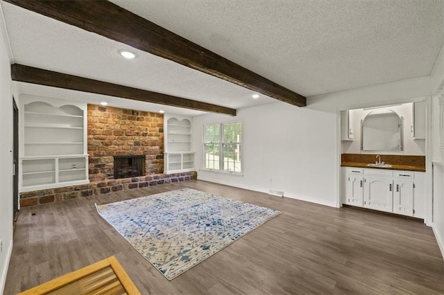 1038 N Woodland Ct, Oakwood, MO 64118 - living room featuring a textured ceiling, dark wood-type flooring, a brick fireplace, baseboards, and beam ceiling