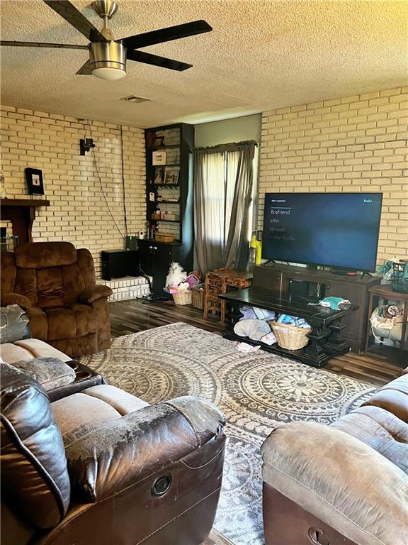 400 S 7th St, Arma, KS 66712 - living room featuring wood finished floors, brick wall, a ceiling fan, and a textured ceiling