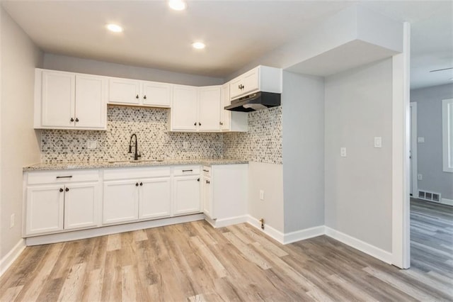 7119 E 111th Ter, Kansas City, MO 64134 - kitchen featuring a sink, under cabinet range hood, light wood-type flooring, white cabinetry, and backsplash