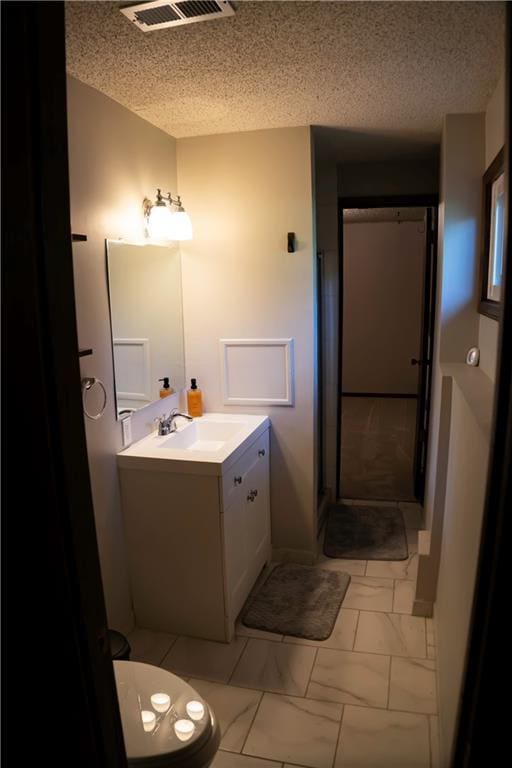 1015 S Elm St, Ottawa, KS 66067 - bathroom featuring a textured ceiling, vanity, marble look tiles, and toilet