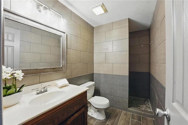 7407 W 145th Ter, Overland Park, KS 66223 - bathroom featuring toilet, vanity, a tile shower, tile walls, and wood finished floors