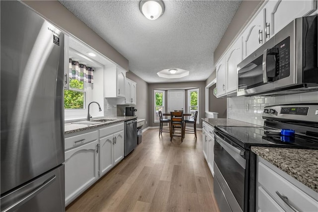 1728 SE 7th Ter, Lees Summit, MO 64063 - kitchen featuring appliances with stainless steel finishes, a sink, white cabinets, light wood-type flooring, and backsplash