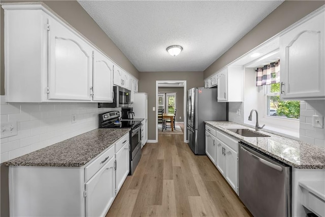 1728 SE 7th Ter, Lees Summit, MO 64063 - kitchen featuring appliances with stainless steel finishes, a sink, white cabinetry, light wood-style floors, and backsplash