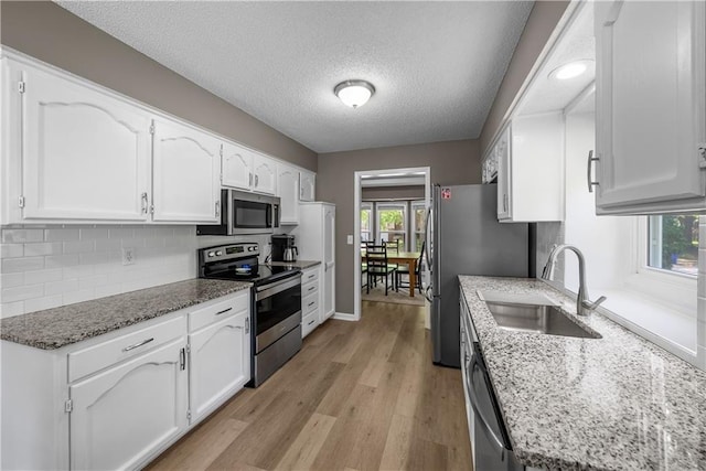 1728 SE 7th Ter, Lees Summit, MO 64063 - kitchen featuring stainless steel appliances, a sink, white cabinets, light wood finished floors, and backsplash