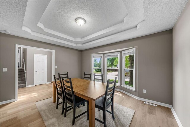 1728 SE 7th Ter, Lees Summit, MO 64063 - dining room featuring a textured ceiling, a tray ceiling, baseboards, light wood finished floors, and stairs