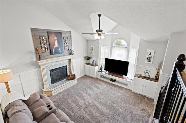 8801 NE 116th St, Kansas City, MO 64157 - carpeted living area featuring a decorative wall, a tiled fireplace, vaulted ceiling, a ceiling fan, and a textured ceiling