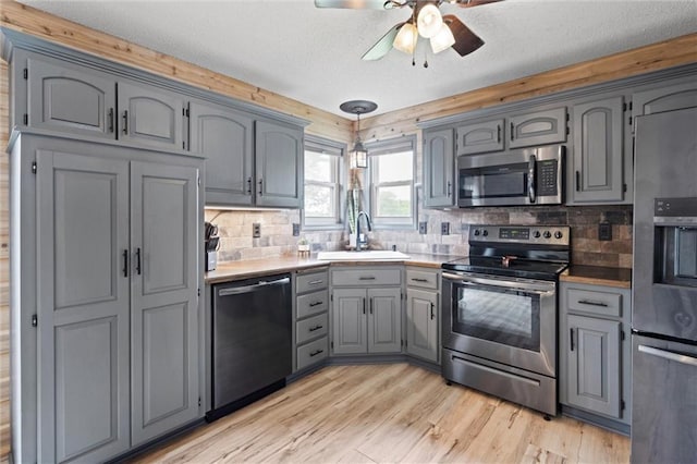 8801 NE 116th St, Kansas City, MO 64157 - kitchen with appliances with stainless steel finishes, gray cabinetry, light wood-style flooring, a ceiling fan, and decorative backsplash