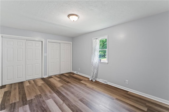 2204 S Cedar Ave, Independence, MO 64052 - unfurnished bedroom featuring multiple closets, baseboards, wood finished floors, and a textured ceiling