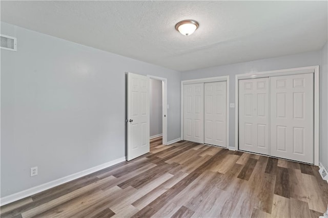 2204 S Cedar Ave, Independence, MO 64052 - unfurnished bedroom with multiple closets, baseboards, wood finished floors, and a textured ceiling