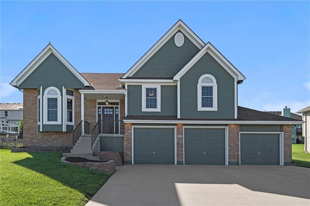 413 Bayview Dr, Raymore, MO 64083 - view of front of property featuring driveway, a front lawn, a garage, and brick siding