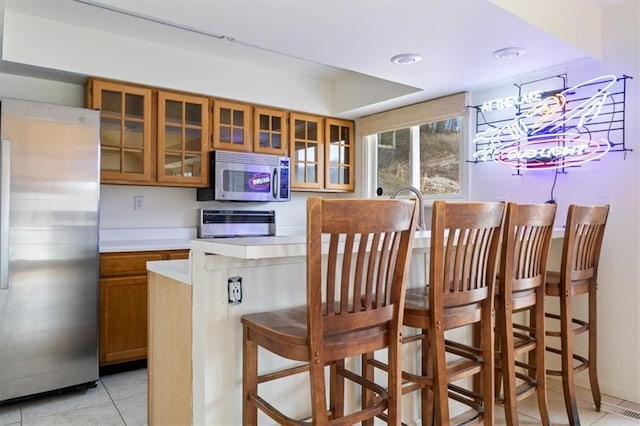 1145 Camp Branch Rd, Sunrise Beach, MO 65079 - kitchen with appliances with stainless steel finishes, brown cabinetry, light tile patterned floors, light countertops, and glass insert cabinets