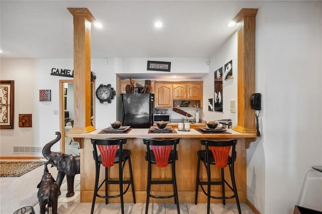 15471 Cedar Ln, Basehor, KS 66007 - kitchen featuring freestanding refrigerator, a peninsula, decorative columns, a kitchen bar, and recessed lighting
