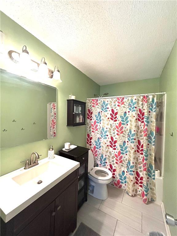 3408 67th St, Kansas City, MO 64119 - bathroom featuring vanity, toilet, a textured ceiling, shower / bath combination with curtain, and tile patterned floors