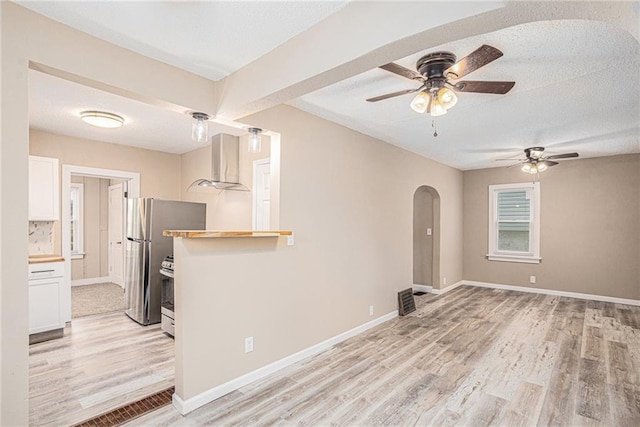 4224 Monroe Ave, Kansas City, MO 64130 - unfurnished living room featuring a ceiling fan, arched walkways, light wood finished floors, baseboards, and a textured ceiling