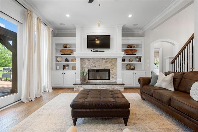 15618 Meadowbrook Ct, Raymore, MO 64083 - living room with crown molding, light wood-style flooring, a stone fireplace, arched walkways, and recessed lighting