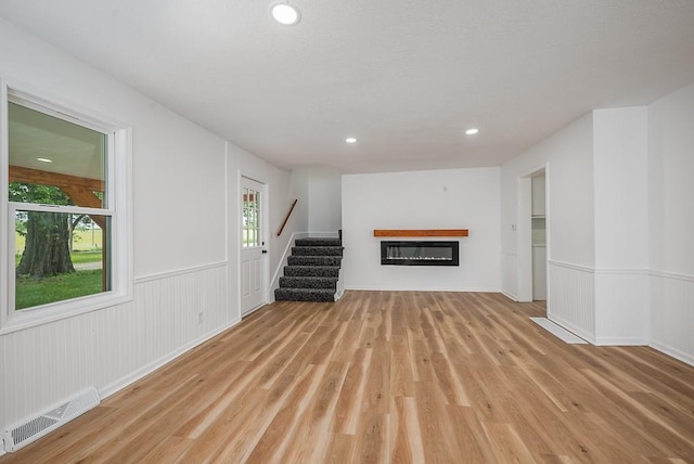 23852 Haigwood Rd, Tonganoxie, KS 66086 - unfurnished living room featuring light wood-style floors, stairway, wainscoting, a glass covered fireplace, and recessed lighting