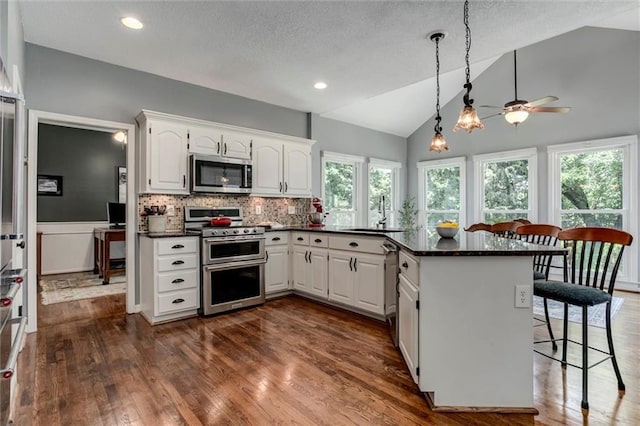 14169 W 115th Ter, Olathe, KS 66062 - kitchen featuring appliances with stainless steel finishes, a peninsula, a kitchen breakfast bar, dark wood-type flooring, and white cabinetry