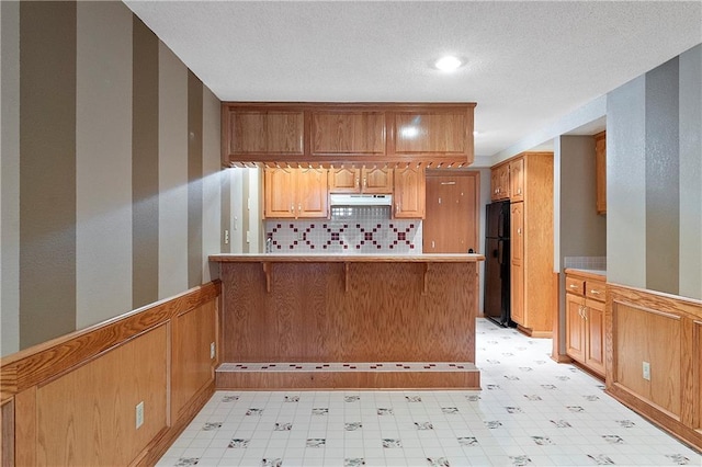11207 W 109th St, Overland Park, KS 66210 - kitchen with under cabinet range hood, freestanding refrigerator, a peninsula, backsplash, and a wainscoted wall
