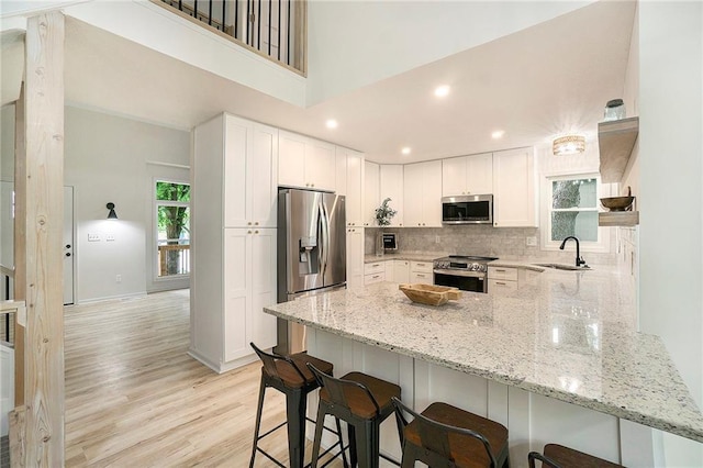 1345 NE Foxwood Dr, Lees Summit, MO 64086 - kitchen featuring appliances with stainless steel finishes, a sink, a peninsula, light stone counters, and a kitchen breakfast bar