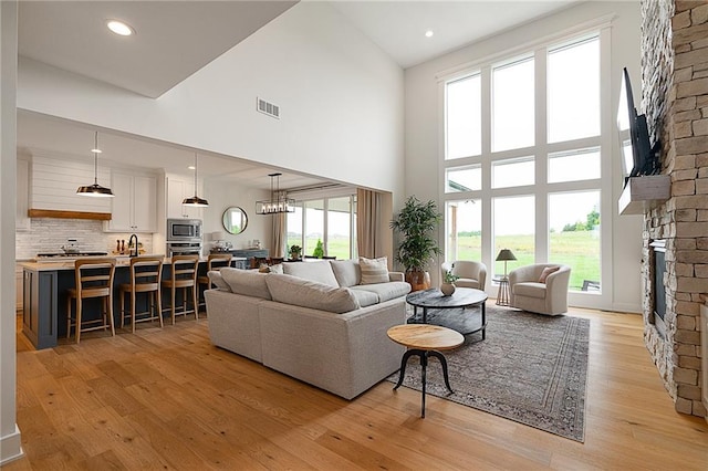 1120 Hillswick Ln, Raymore, MO 64083 - living room featuring a fireplace, a towering ceiling, light wood-type flooring, a chandelier, and recessed lighting