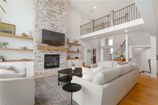 1120 Hillswick Ln, Raymore, MO 64083 - living room with a towering ceiling, light wood finished floors, a stone fireplace, stairs, and baseboards