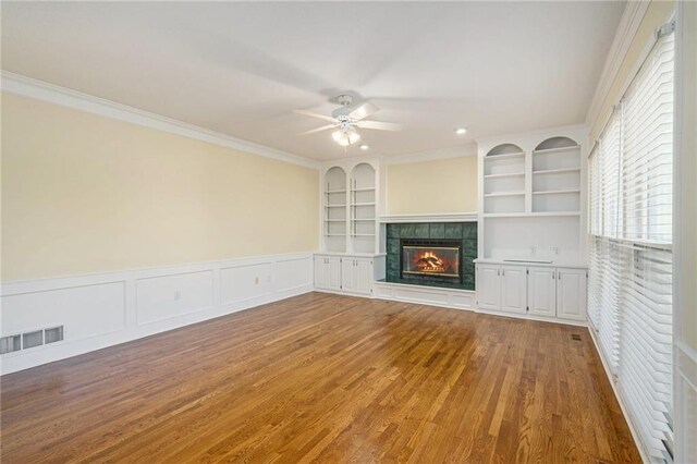 8901 W 128th St, Overland Park, KS 66213 - unfurnished living room with wood finished floors, a ceiling fan, a tiled fireplace, crown molding, and built in features