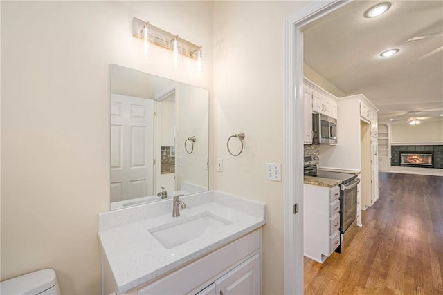 8901 W 128th St, Overland Park, KS 66213 - bathroom featuring vanity, wood finished floors, a ceiling fan, toilet, and a glass covered fireplace