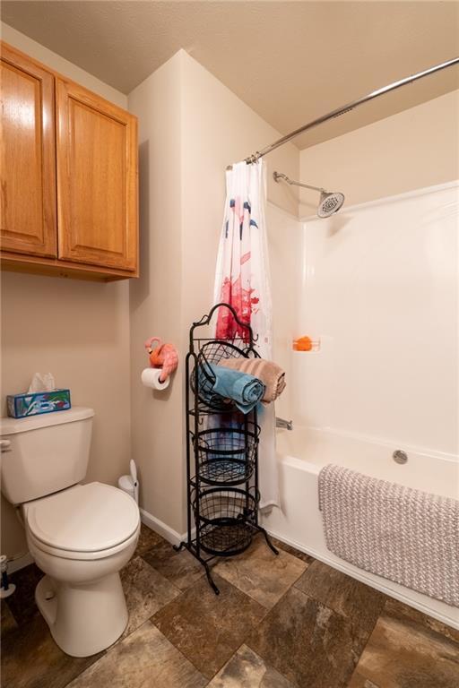 2943 NE Turkey Rd, Breckenridge, MO 64625 - bathroom featuring stone finish flooring, toilet, shower / bathtub combination with curtain, and baseboards