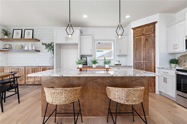 20786 Emerald St, Spring Hill, KS 66083 - kitchen with stainless steel electric range, light wood-type flooring, a kitchen island, white cabinetry, and a breakfast bar area