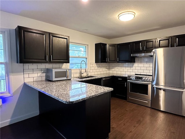 609 N Broadway St, Knob Noster, MO 65336 - kitchen featuring stainless steel appliances, a sink, under cabinet range hood, light stone countertops, and a peninsula