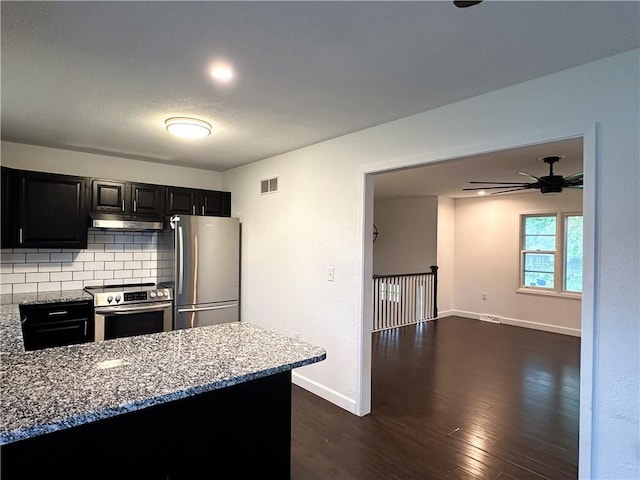 609 N Broadway St, Knob Noster, MO 65336 - kitchen with appliances with stainless steel finishes, under cabinet range hood, baseboards, dark cabinetry, and decorative backsplash