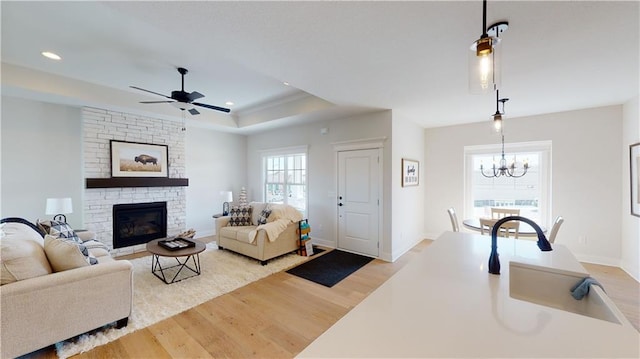 15595 N Sheridan Ct, Basehor, KS 66007 - living area featuring light wood-style floors, a tray ceiling, a stone fireplace, a chandelier, and a ceiling fan