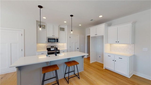 15595 N Sheridan Ct, Basehor, KS 66007 - kitchen featuring stainless steel appliances, decorative backsplash, white cabinets, light wood finished floors, and an island with sink