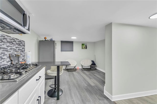 2831 E 8th St, Kansas City, MO 64124 - kitchen with dark countertops, light wood finished floors, baseboards, stainless steel gas cooktop, and decorative backsplash