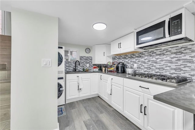 2831 E 8th St, Kansas City, MO 64124 - kitchen with estacked washer and dryer, stainless steel gas stovetop, a sink, decorative backsplash, and light wood finished floors