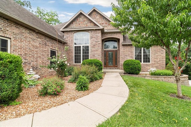 906 Cheatham Ct, Warrensburg, MO 64093 - view of exterior entry featuring brick siding, a yard, and roof with shingles