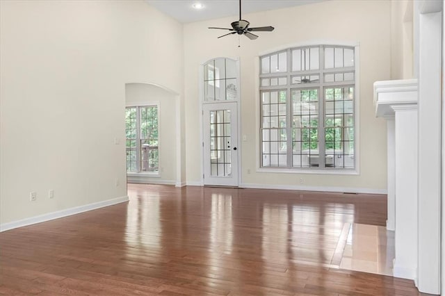 906 Cheatham Ct, Warrensburg, MO 64093 - unfurnished living room featuring ceiling fan, wood finished floors, baseboards, arched walkways, and a high ceiling