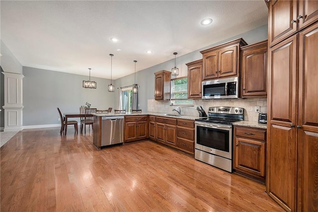 5021 NW Timberline Dr, Riverside, MO 64150 - kitchen featuring appliances with stainless steel finishes, tasteful backsplash, a peninsula, hanging light fixtures, and light stone countertops