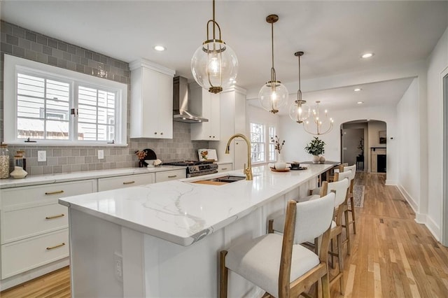 4804 Jarboe St, Kansas City, MO 64112 - kitchen featuring wall chimney range hood, arched walkways, tasteful backsplash, white cabinets, and a sink