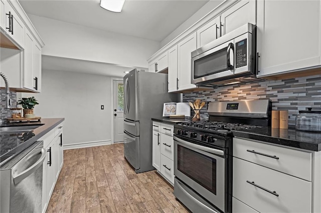4421 Tracy Ave, Kansas City, MO 64110 - kitchen with stainless steel appliances, a sink, white cabinets, decorative backsplash, and light wood-style floors